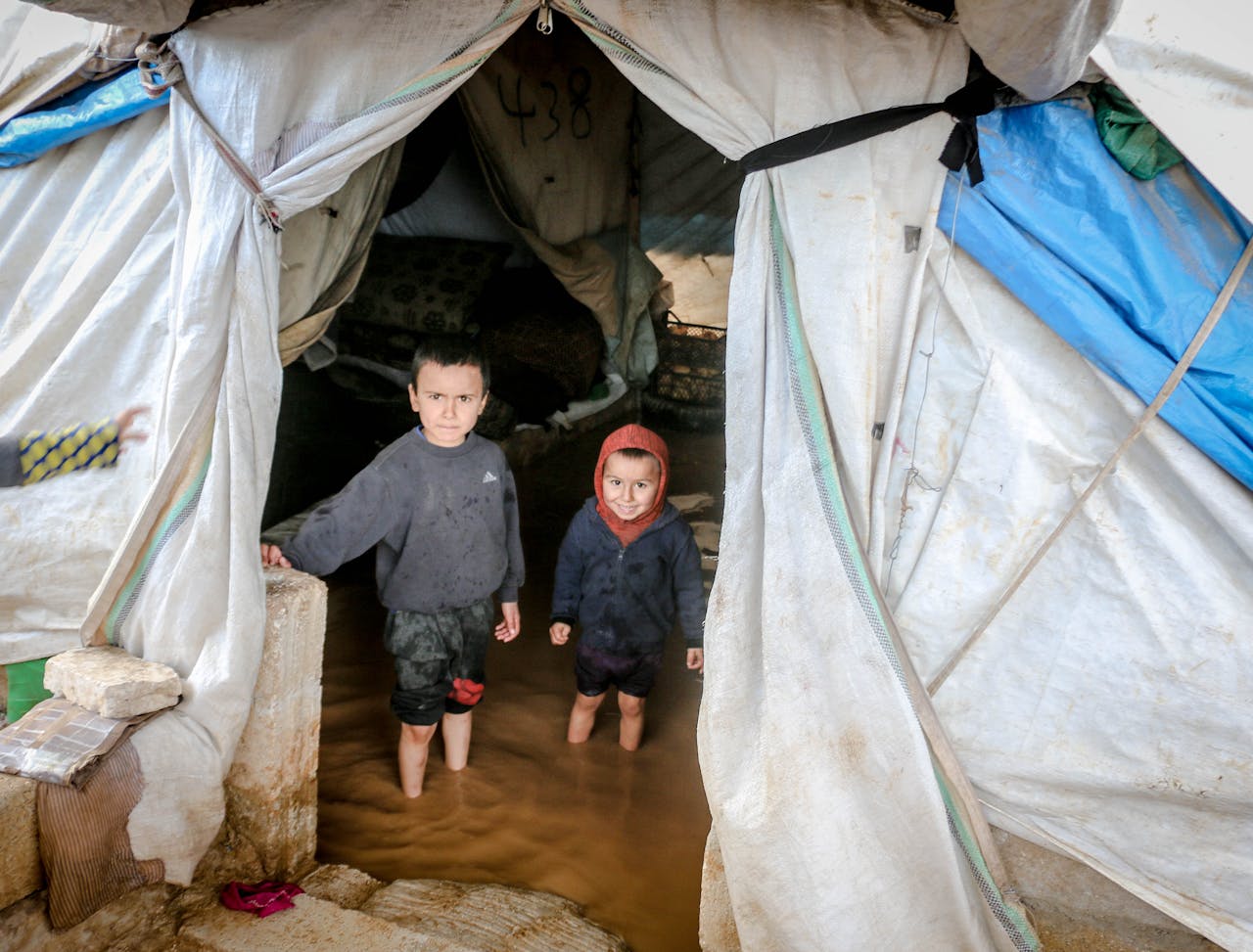 Two young children stand in a flooded tent in Idlib, Syria, highlighting the hardships in refugee camps.