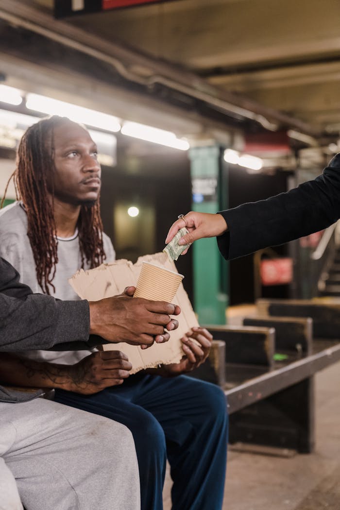 A man gives money to a homeless person sitting in a subway station.